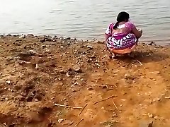 Indian woman urinating in the dirt by a lake
