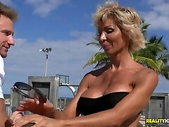 Stacked MILF in a thong at the beach ravages a younger boy