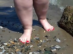 Fat bare legs with red pedicure walk along the bank of the river, fetish.