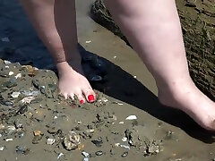 Fat bare legs with red pedicure walk along the bank of the river, fetish.