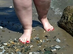 Fat nude legs with red pedicure walk along the bank of the river, fetish.